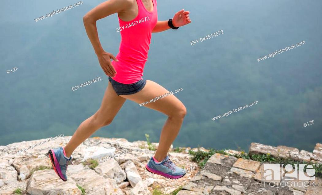 Stock Photo: young woman trail runner running on great wall on the top of mountain.