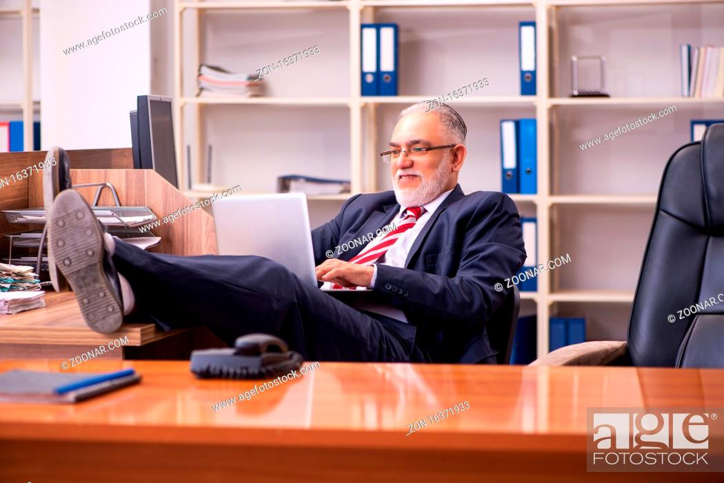 Stock Photo: Old male employee sitting at workplace.