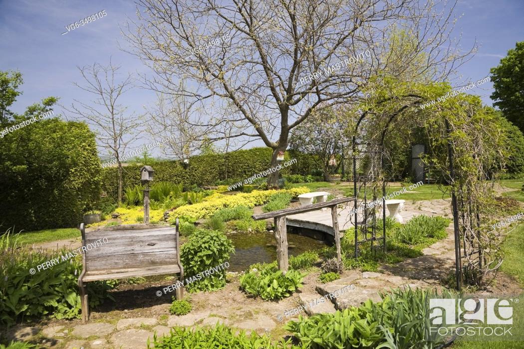 Stock Photo: Flagstone path with old wooden sitting bench and black metal arbour in backyard country garden in spring.