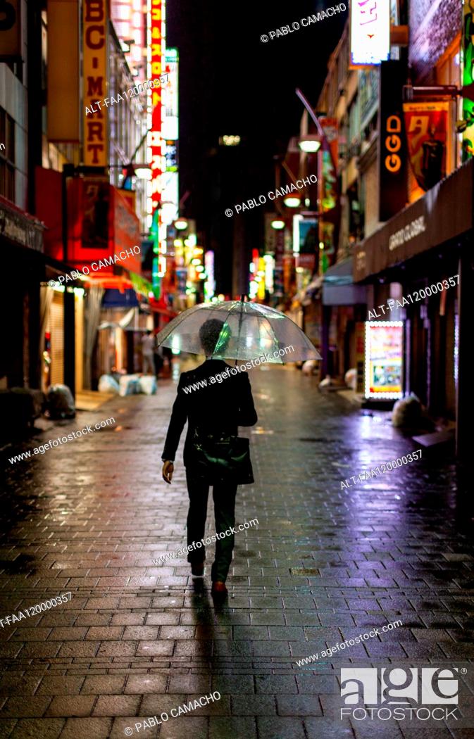 Stock Photo: Man walking in rain with umbrella at night.