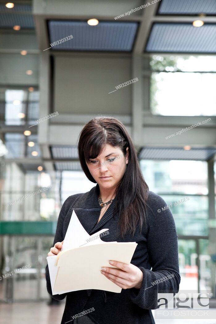 Photo de stock: A young Caucasian businesswoman going through paperwork in a convention centre lobby area.