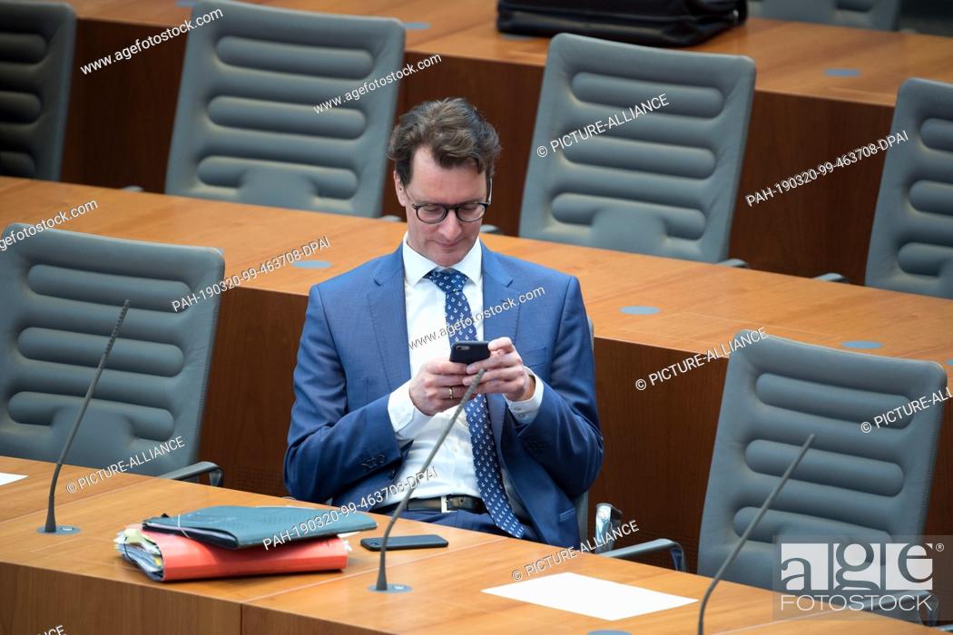 Stock Photo: 20 March 2019, North Rhine-Westphalia, Düsseldorf: Hendrik Wüst (CDU), Transport Minister of North Rhine-Westphalia, looks at his mobile phone in plenary.