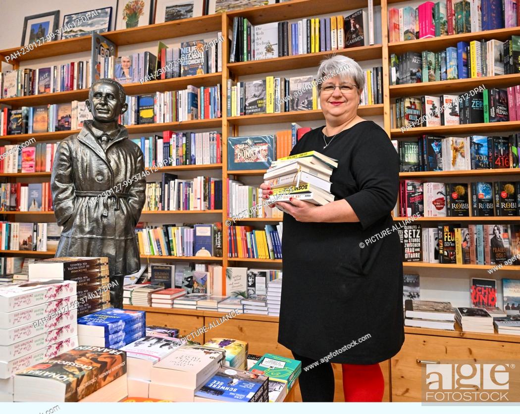 Stock Photo: PRODUCTION - 18 January 2023, Brandenburg, Bernau: Sylvia Pyrlik, bookseller and owner of the ""Schatzinsel"" bookstore, stands next to a figure by playwright.
