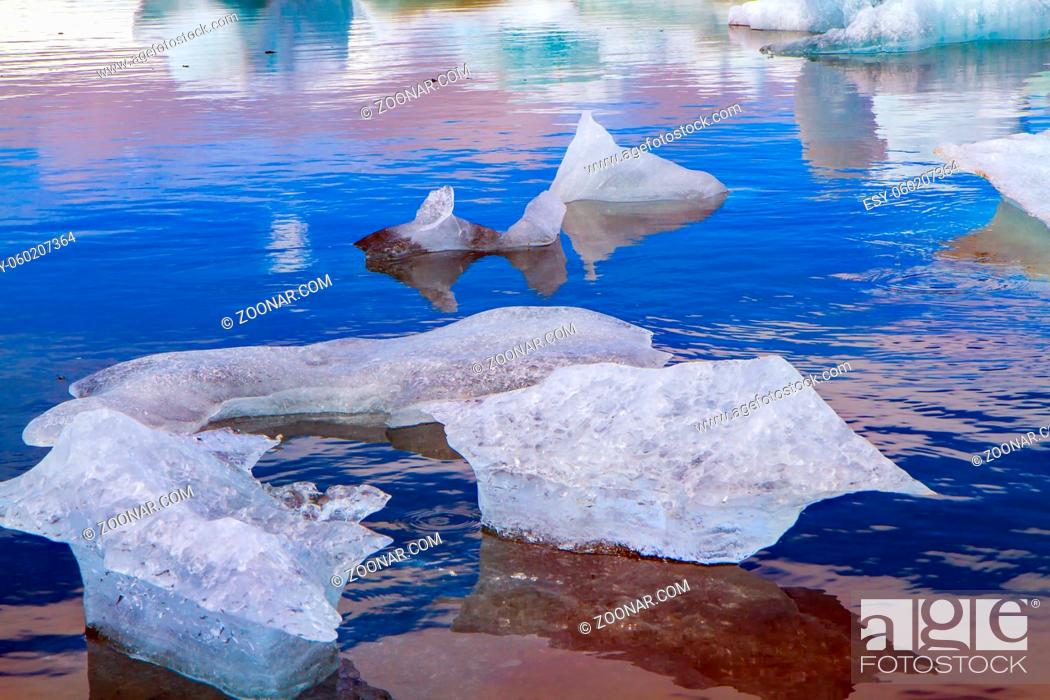 Stock Photo: Cold July day. Bizarre icebergs and floating ice floes reflected in the smooth cold water of the lagoon. The lagoon Jokulsaurloun. Iceland.