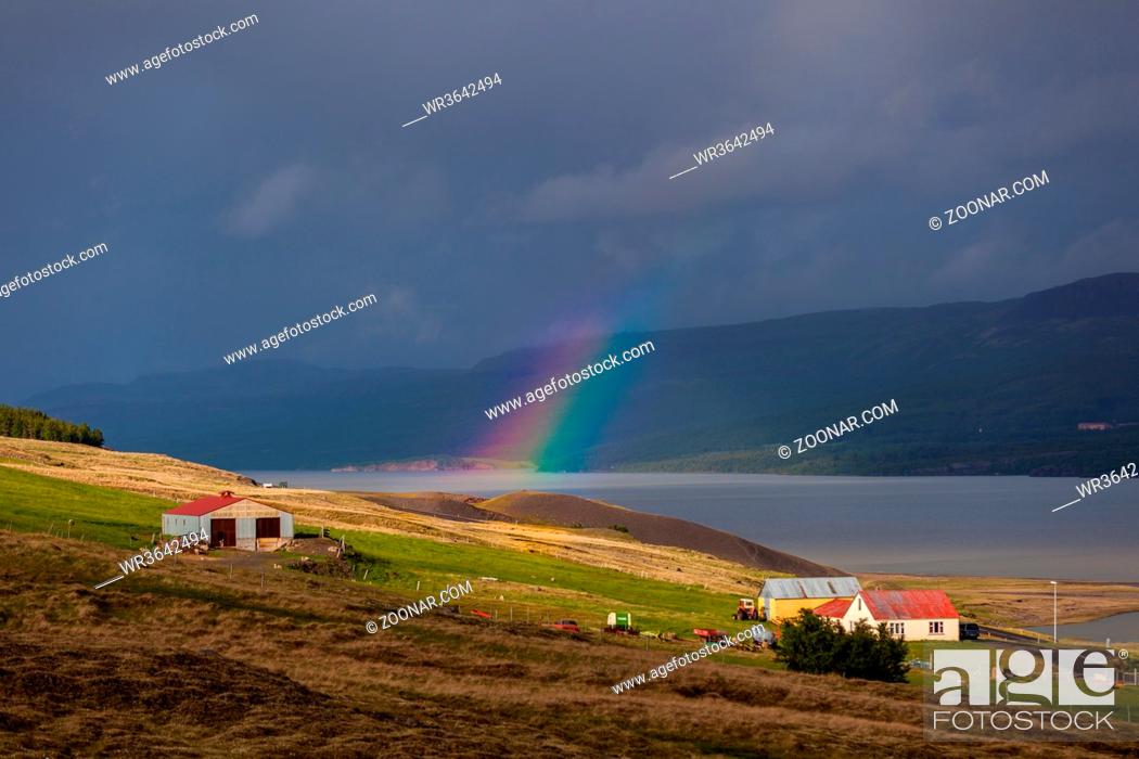 Stock Photo: rainbow expanding over a wide river in a valley with a small white and red farm building on Iceland.
