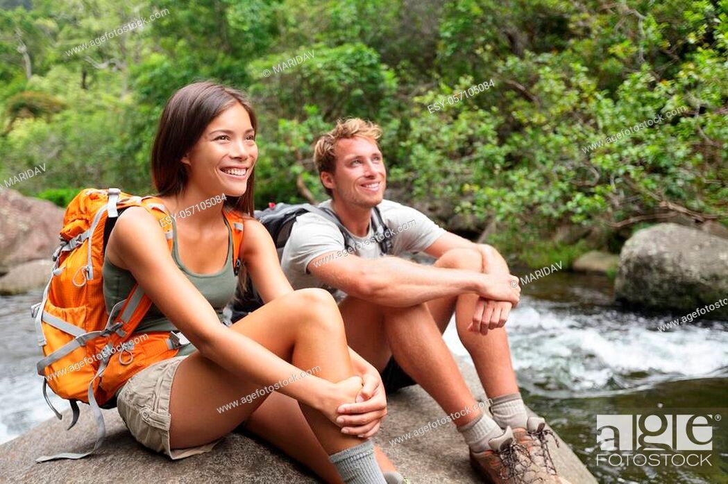 Stock Photo: Hikers couple relaxing by river enjoying outdoor activity wearing backpacks sitting down. Woman and man hiker looking with smiling happy.