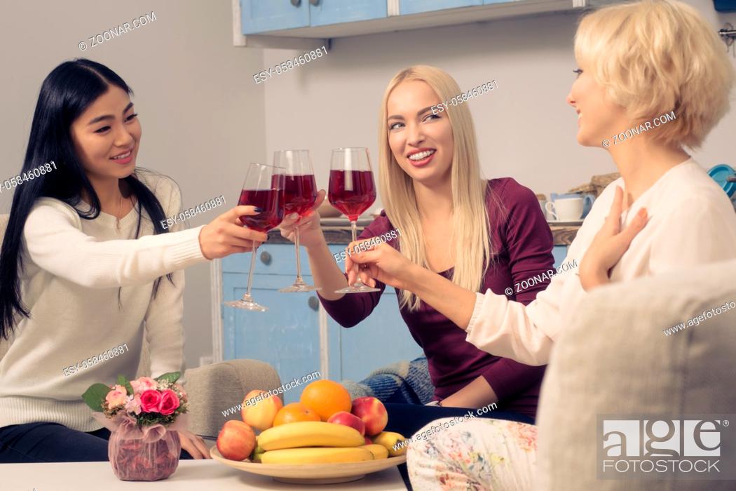 Stock Photo: Toned picture of happy friends girls drinking red wine and smiling while spending free time at home. Beautiful cheerful ladies having party in kitchen after.