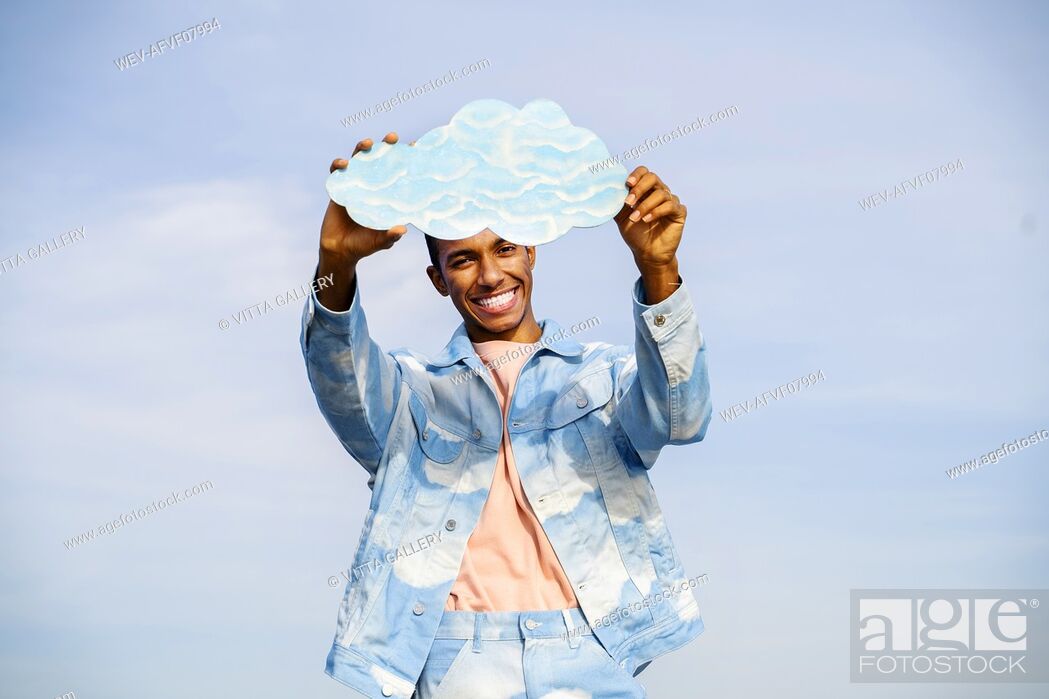 Stock Photo: Smiling young man holding cloud while standing against sky.