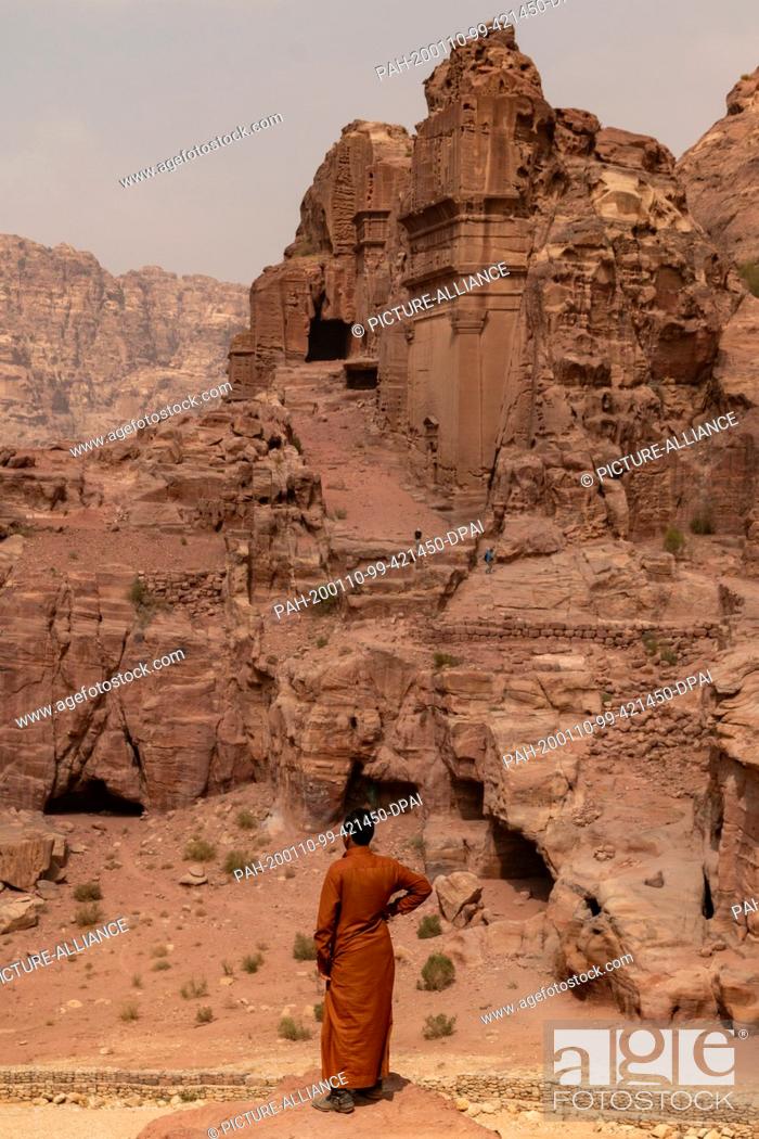 Stock Photo: 19 October 2018, Jordan, Petra: A Bedouin looks down from a rock on the ancient city of Petra. In the background the El Khoubta mountains can be seen.