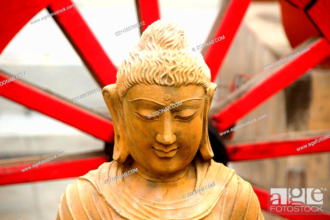 Stock Photo: Calm, quiet, wise and serene face of Buddha sitting with red spiked wheel in the background.