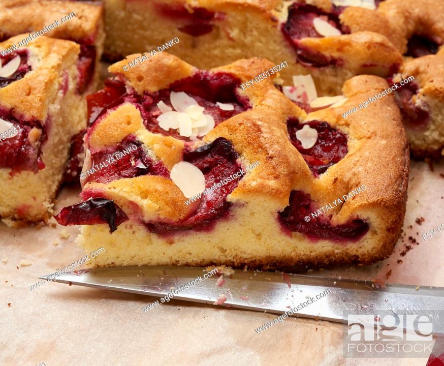 Stock Photo: baked slices of sponge cake with plums on brown paper and a knife, close up.