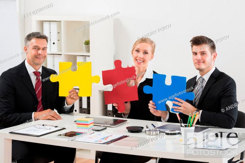 Stock Photo: Team Of Happy Businesspeople Holding Multi-colored Jigsaw Puzzle In Office.