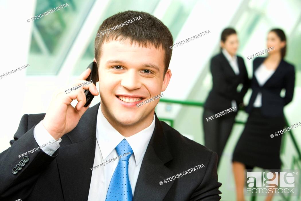 Stock Photo: Portrait of a young successful businessman making business call on mobile looking at camera on the background of two standing women.