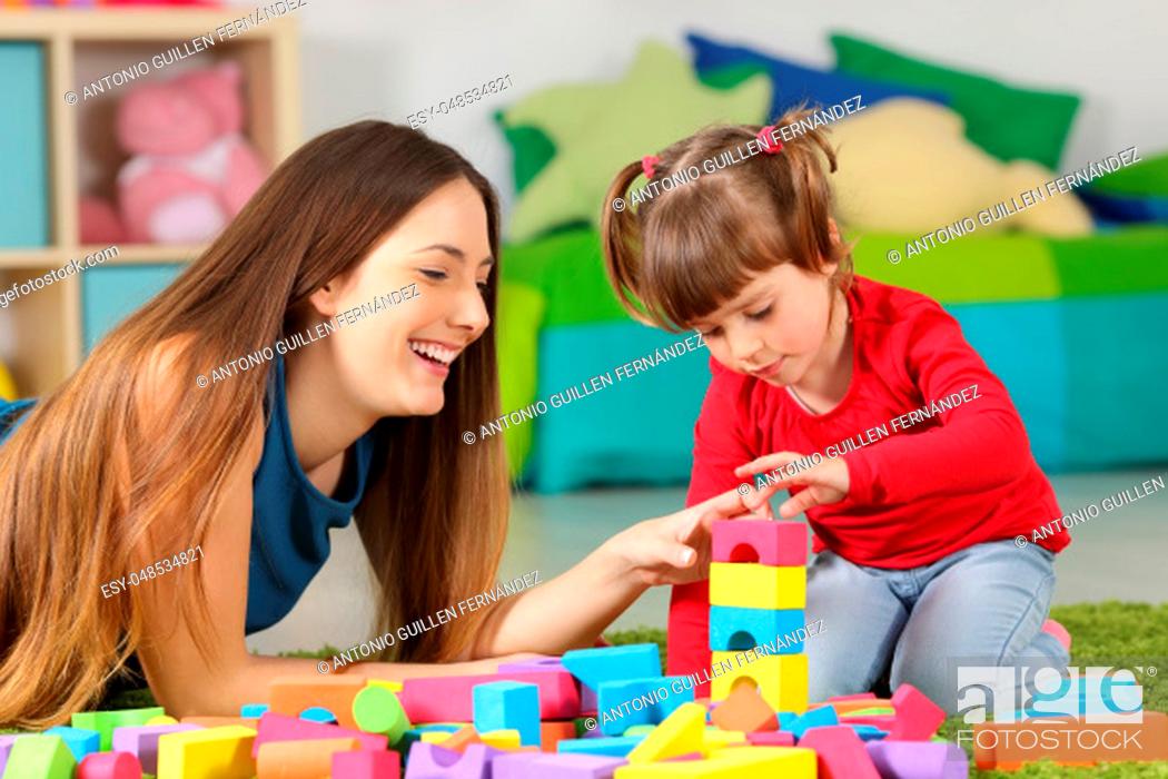Stock Photo: Mother and daughter playing together with colorful construction toys on a carpet on the floor af a bedroom at home.