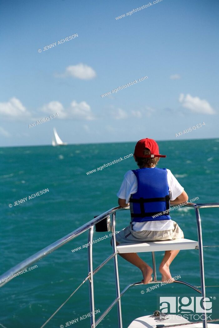 Stock Photo: Boy in life vest sitting on edge of sailboat.