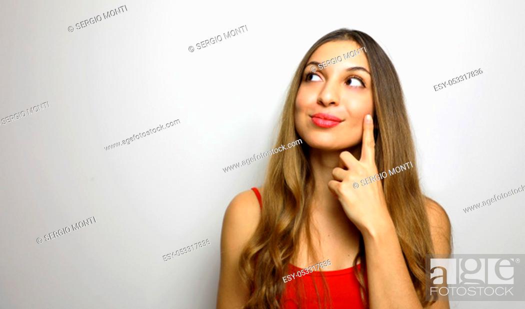 Imagen: I have great idea! Studio shot of attractive female moving fingers near cheek as if making up plan in mind, smiling while looking happy aside.