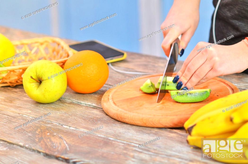 Stock Photo: Hands of young girl in sportswear cutting kiwi on chopping board and listens to music.