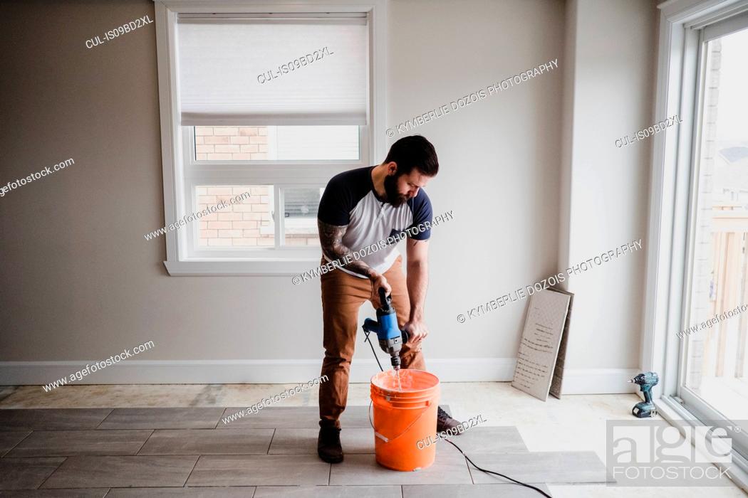 Stock Photo: Man mixing cement in bucket with hand mixer.