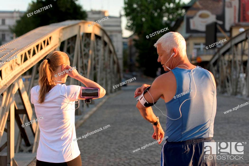 Stock Photo: jogging couple check music playlist on phone and plan route before morning running workout with sunrise in the city and sun flare in background.