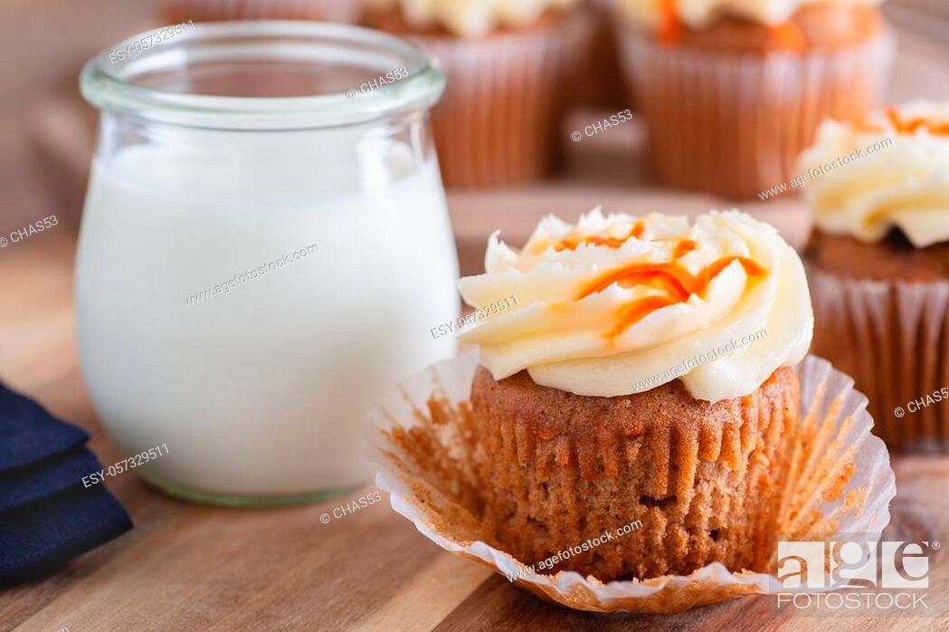 Stock Photo: Closeup of carrot cupcake with cream cheese icing and glass of milk and cupcakes in background.