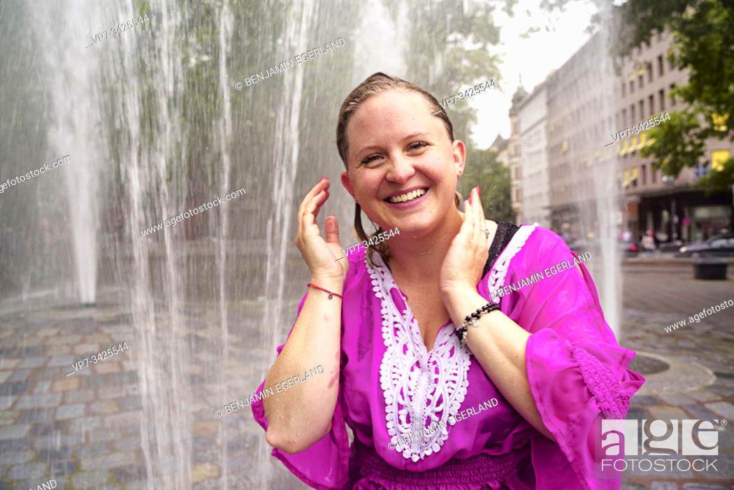 Stock Photo: Woman under fountain water spray, Munich, Germany.
