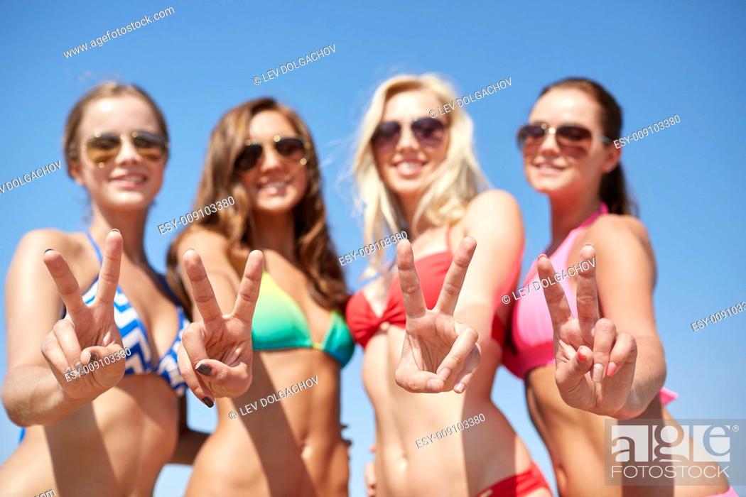 Stock Photo: summer vacation, holidays, gesture, travel and people concept - group of smiling young women showing peace or victory sign over blue sky background.