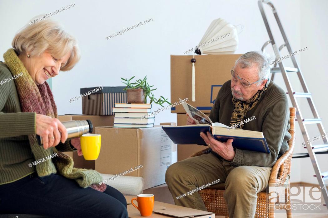 Stock Photo: Senior couple with photo album and hot drink surrounded by cardboard boxes in an empty room.