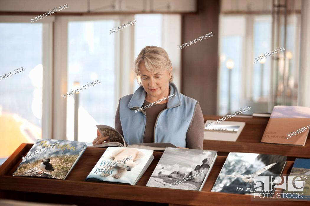 Stock Photo: Woman looking at book in library on cruise ship sailing the British Isles.