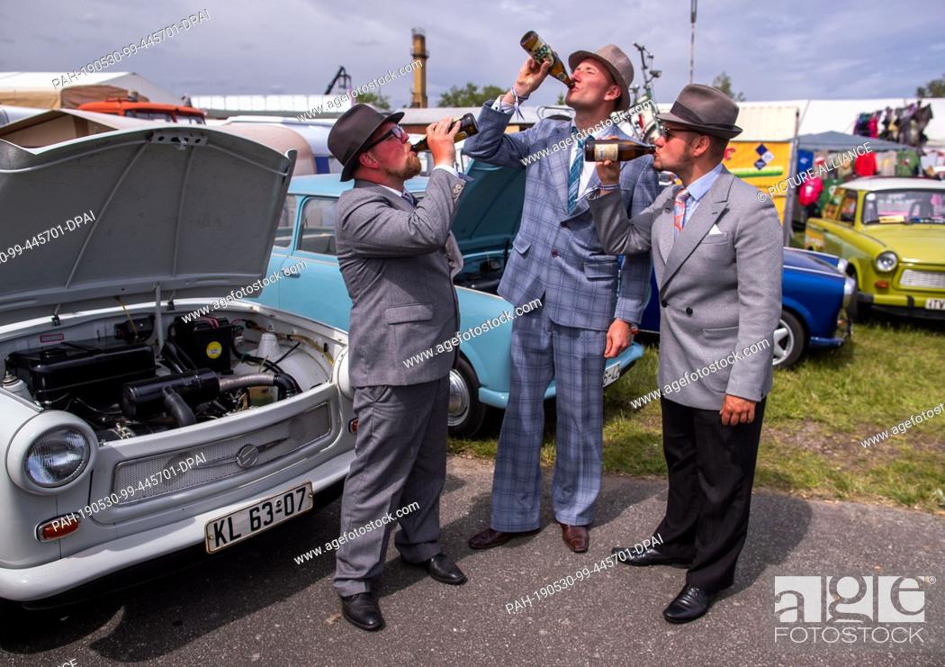 Stock Photo: 30 May 2019, Mecklenburg-Western Pomerania, Anklam: In front of their vehicles, three festively dressed gentlemen drink from their beer bottles on Father's Day.