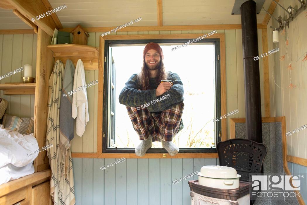 Stock Photo: Portrait happy young man in pajamas in tiny cabin window.