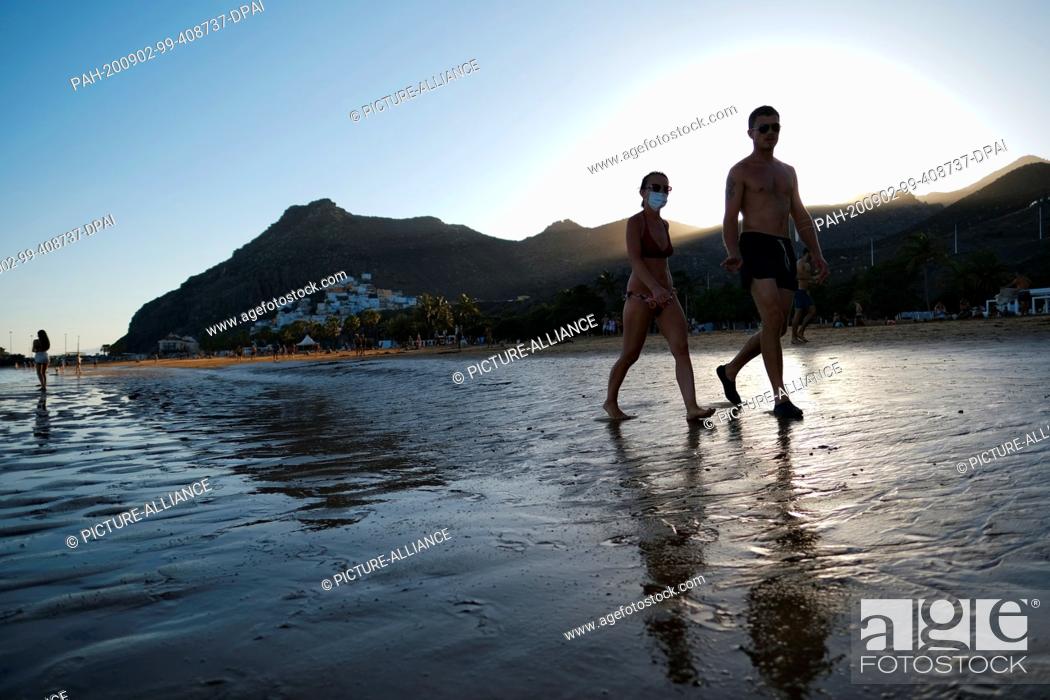 Stock Photo: 02 September 2020, Spain, Santa Cruz: A couple wearing mouthguards is walking on the beach when the federal government classifies the Canary Islands as a risk.