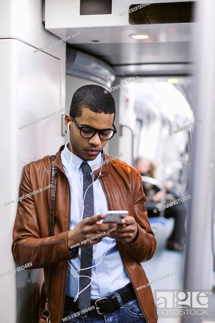 Stock Photo: Businessman with smartphone and earphones hearing music on the subway train.