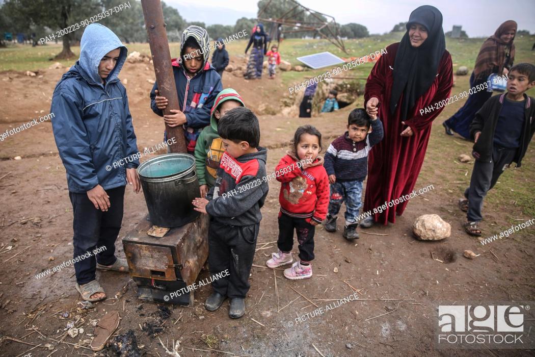 Stock Photo: 23 February 2020, Syria, Idlib: Syrian children and a woman are pictured outside a cave at Taltouna village. At least eight families live in an ancient deserted.