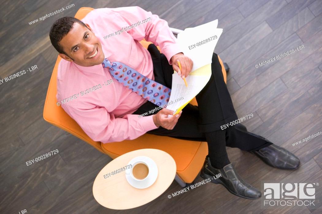 Stock Photo: Businessman sitting indoors with coffee and folder smiling.