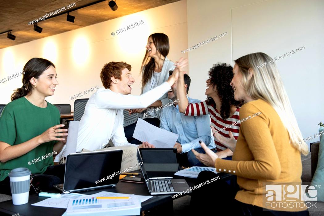 Stock Photo: Colleagues giving high five at a group meeting.