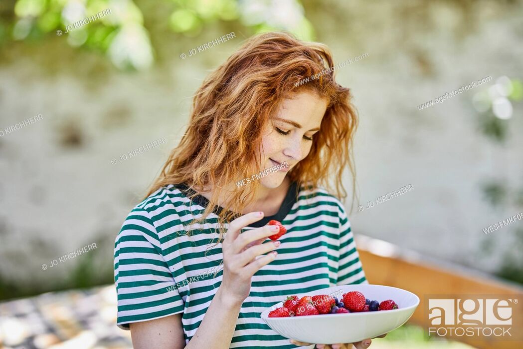 Stock Photo: Portrait of smiling redheaded young woman with bowl of berries in the garden.