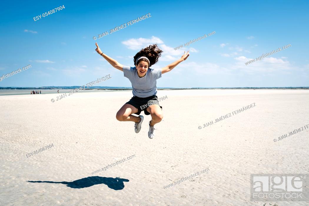 Stock Photo: Full-length portrait of joyful female traveler jumping on the beach in the bay of Mont Saint-Michel.
