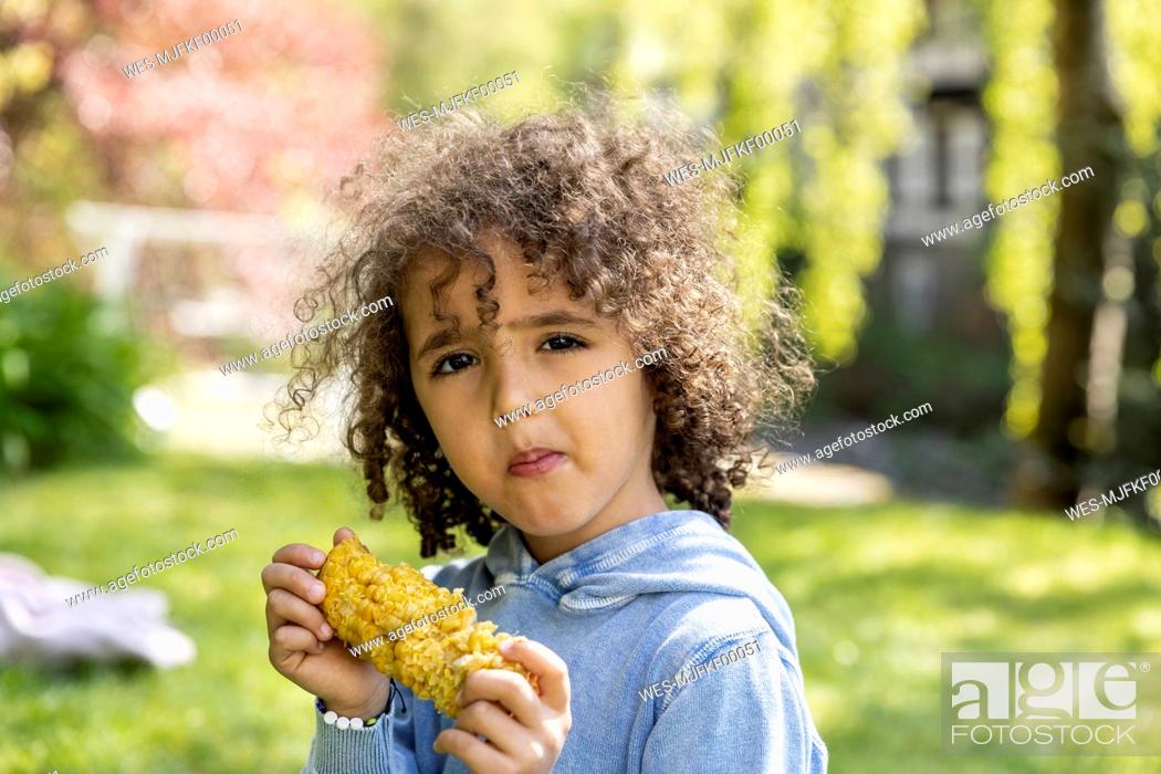 Imagen: Portrait of boy eating a corn cob in garden.