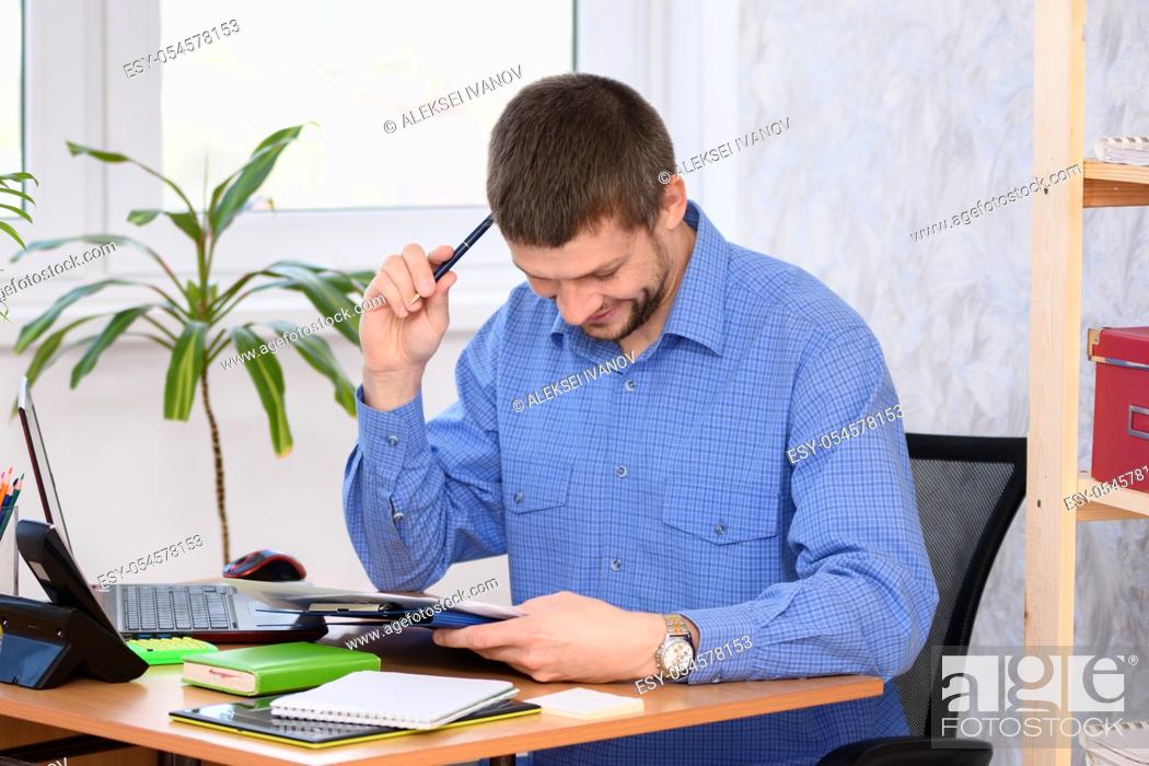 Imagen: Office employee reads a document, smiles and scratches his head with a pen.