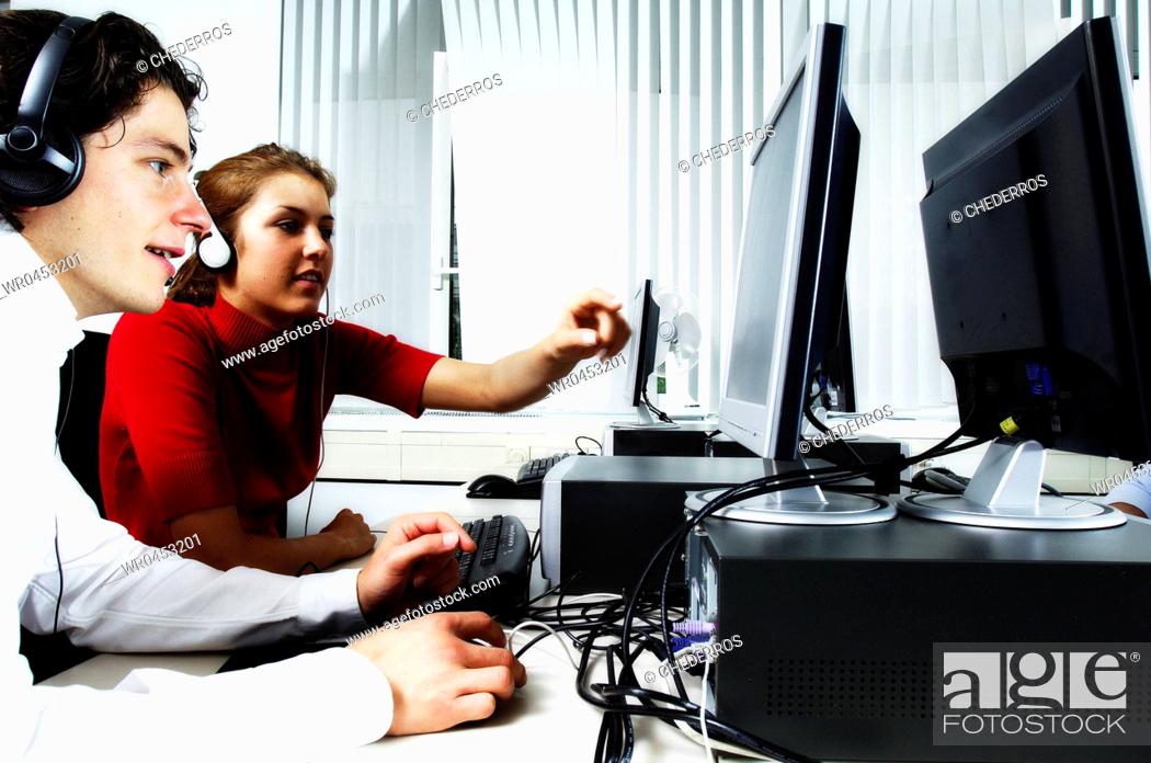 Stock Photo: Teenage girl pointing to a computer with a teenage boy sitting beside her wearing a headset.