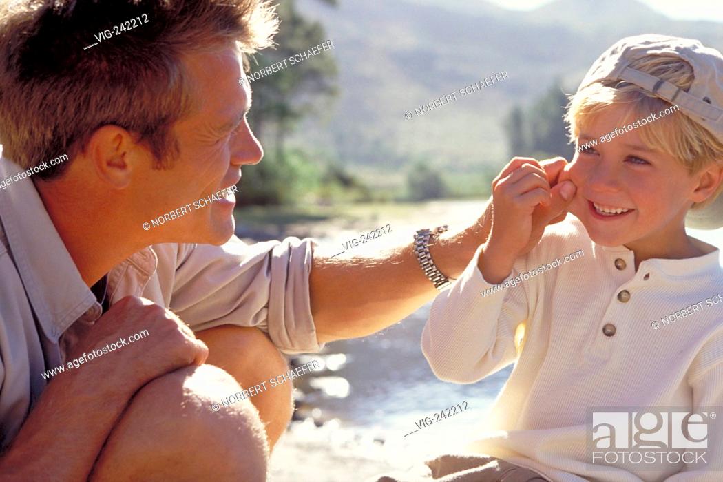 Stock Photo: outdoor, close-up, blond father and his 6-year-old son squad at a shore of a lake in a forest and he is pitching his cheek  - GERMANY, 19/09/2004.