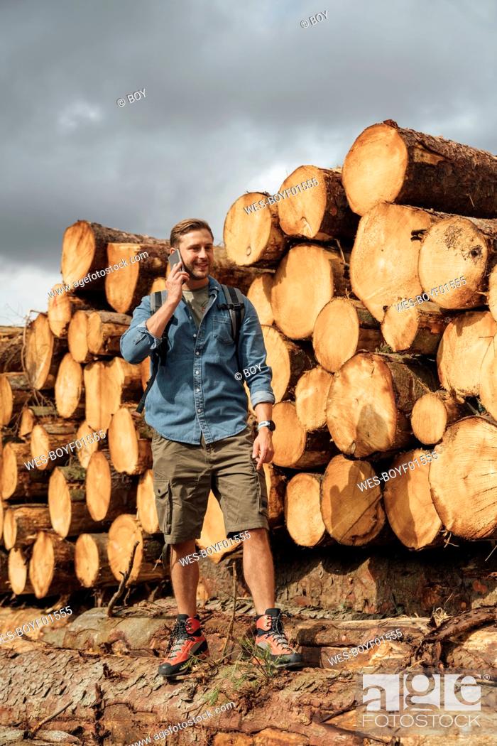 Stock Photo: Mid adult man talking over smart phone while standing by woodpile in forest.