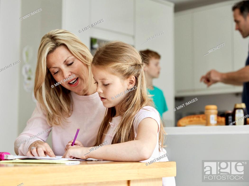 Stock Photo: a woman and her daughter seated at a table in the kitchen looking at her homework.