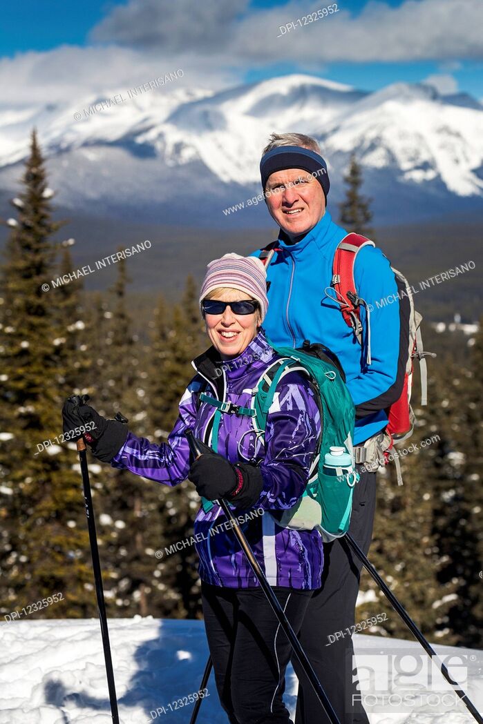 Stock Photo: Male and female cross country skiiers on a lookout with snow covered mountains, blue sky and clouds in the background; Lake Louise, Alberta, Canada.
