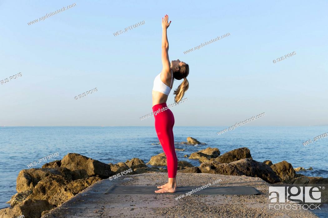 Stock Photo: Young woman practicing yoga on the beach, doing sun salutations.