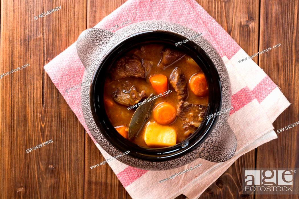 Stock Photo: Meat stew with vegetables in ceramic pot on wooden table. Top view.