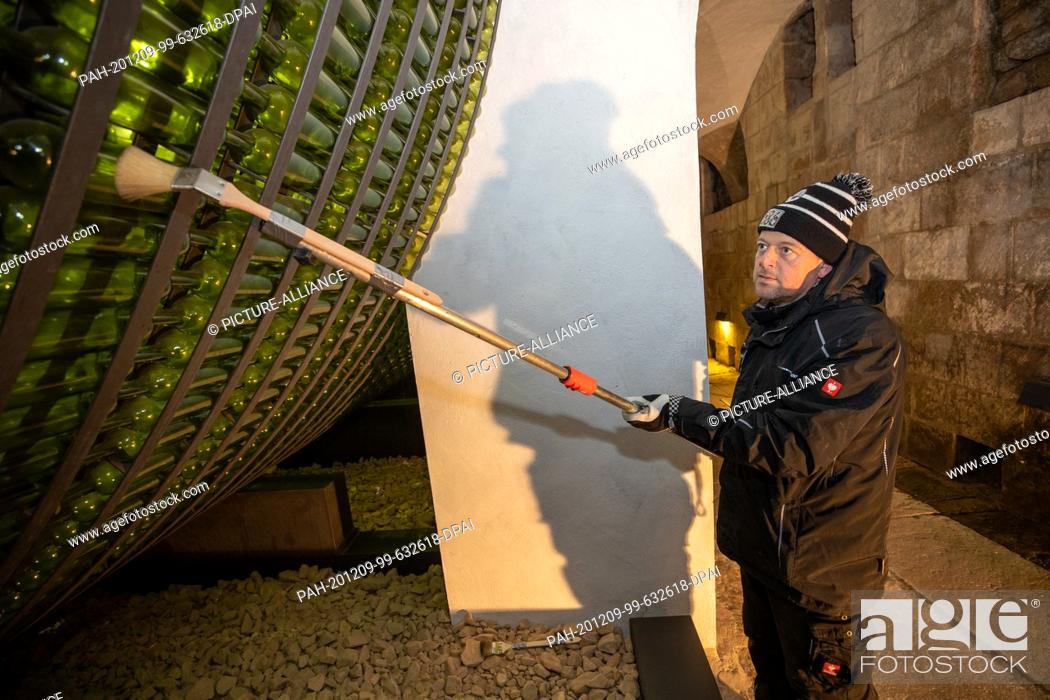 Stock Photo: 04 December 2020, Saxony, Königstein: Jens Hickmann cleans with a brush and an extension from the outside over the wine bottles.