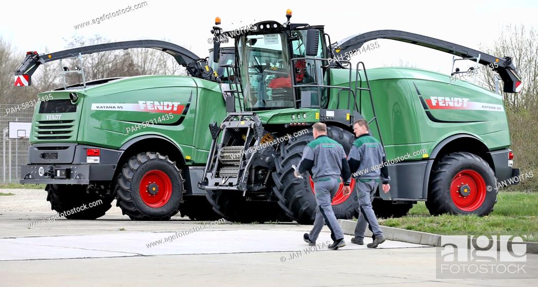 Stock Photo: Two employees walk past a Fendt Katana 65 corn chopper on the compound of former barracks of the German armed forces in Hohenmoelsen, Germany, 17 April 2015.