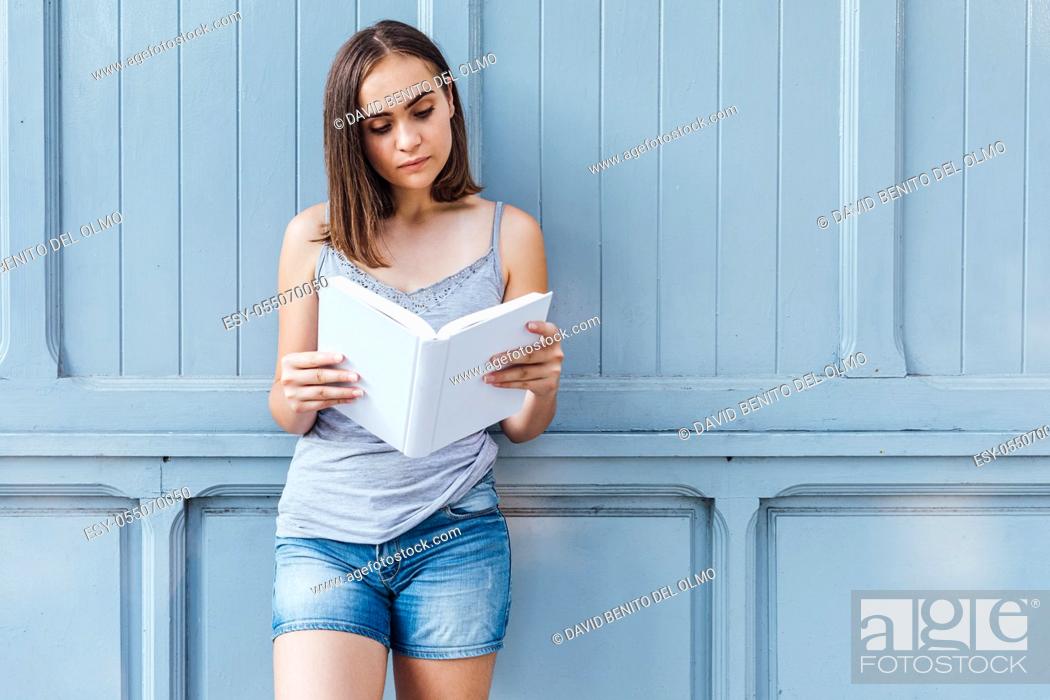 Stock Photo: Young girl reading a book on bluish gray background.