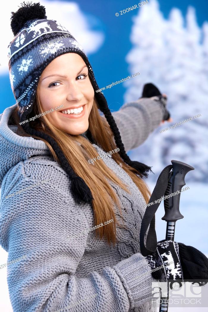 Stock Photo: Attractive young female dressed up warm for skiing wearing cap and gloves smiling and pointing to winter landscape .